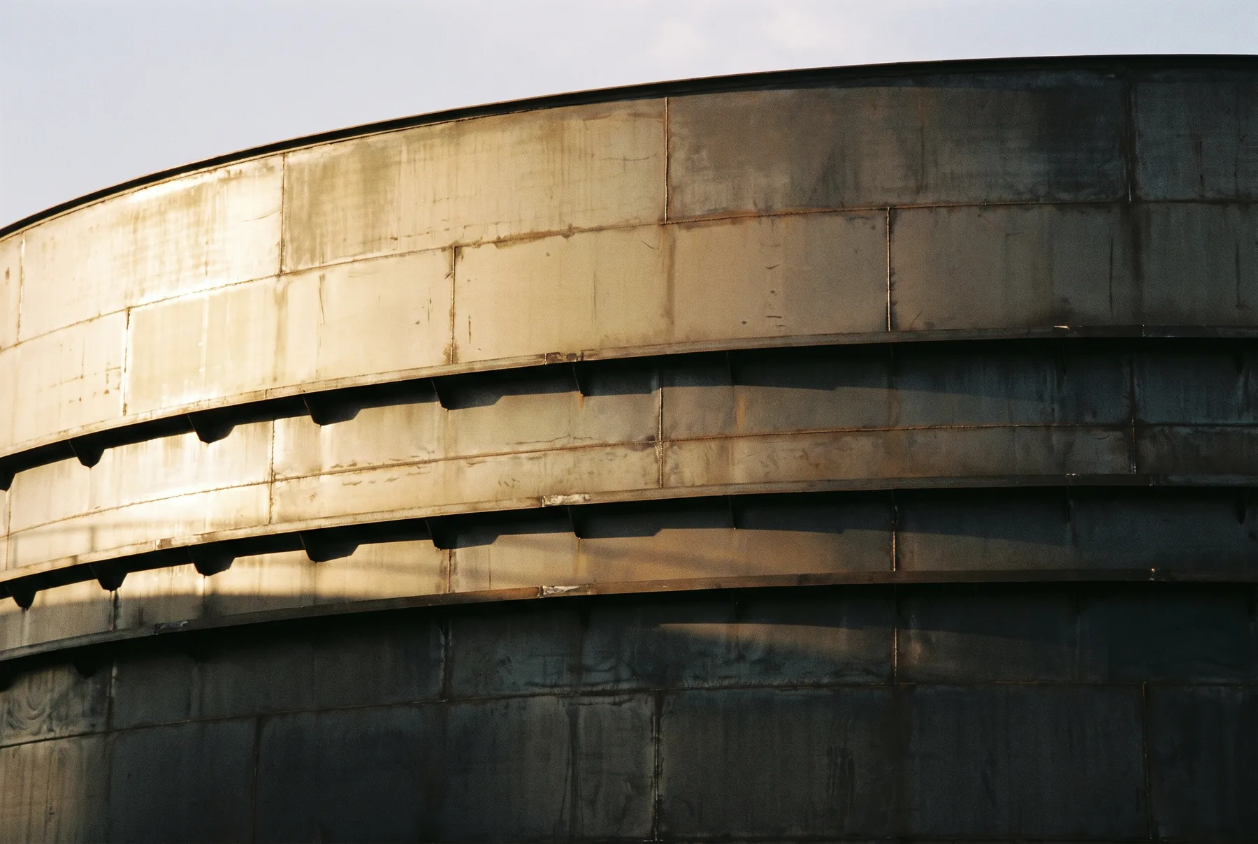 Exterior wall of a cylindrical storage tank in late afternoon light.